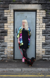 Copywriter Lisa Derrick, and her daschund, standing in front of a blue door.