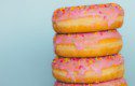A stack of 4 doughnuts with pink icing and hundreds and thousands on top of each one.
