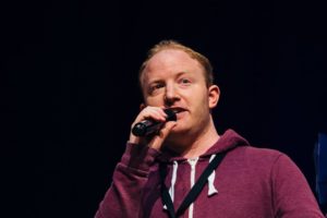Richard Woodhall, copywriter in a burgundy hooded top, holding a microphone to his mouth
