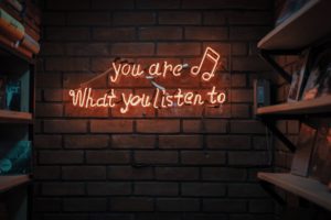 The words 'you are what you listen to' in orange neon lettering on a brick wall.