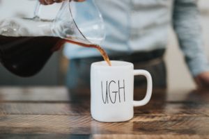 A barista pouring coffee into a mug that says "ugh" on it.