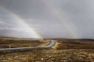 A winding road with 2 rainbows in the background.