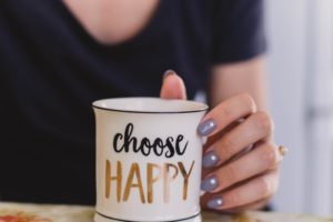 Woman in a black top with a white mug that says "choose happy" on it.