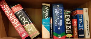 A collection of dictionaries and thesauruses lined up on a bookshelf.