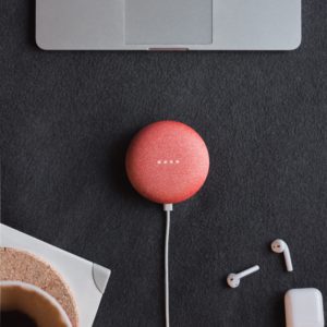 Google Home Mini on a black surface beside some Apple AirPods